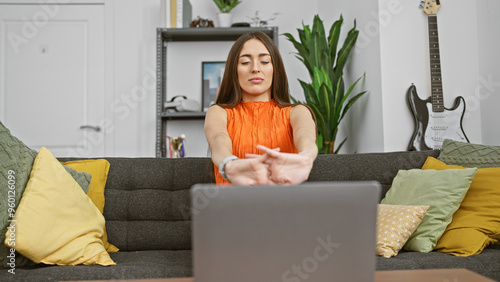 Woman stretching arms during a break from laptop work in a cozy living room with guitar and plants. photo