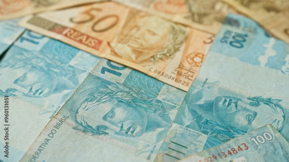 Brazilian banknotes scattered, featuring 10, 50, and 100 reais denominations, representing brazil's currency and financial concept.