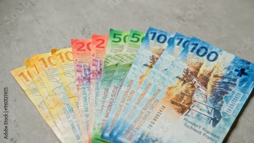 Swiss franc banknotes spread out on a concrete surface, showcasing various denominations including 10, 20, 50, and 100 francs, vibrant colors and intricate design details. photo