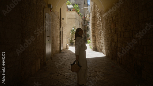 Young hispanic woman exploring the narrow stone streets of bari old town in puglia, italy, on a sunny day.