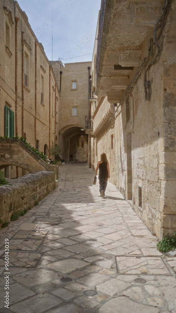Obraz premium Hispanic woman walking through the picturesque old town of matera in basilicata, italy, on a sunny day