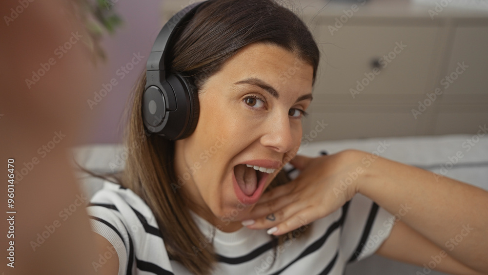 A joyful woman with headphones taking a selfie in a modern apartment living room. A joyful woman with headphones taking a selfie in a modern apartment living room.