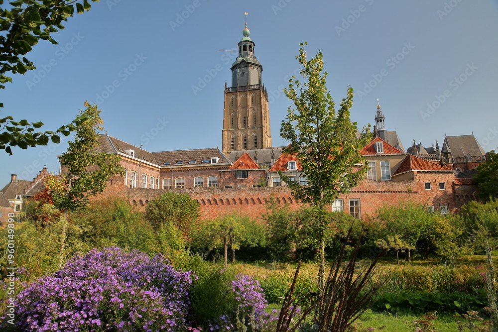 Saint Walburgiskerk church and historic medieval houses surrounded by fortifications in Zutphen, Gelderland, Netherlands, with green gardens and flowers in the foreground