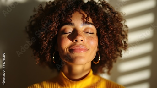 Wallpaper Mural A woman with curly hair dons a yellow top and smiles warmly with eyes closed, basking in sunlight through window blinds, exuding contentment and natural serenity. Torontodigital.ca