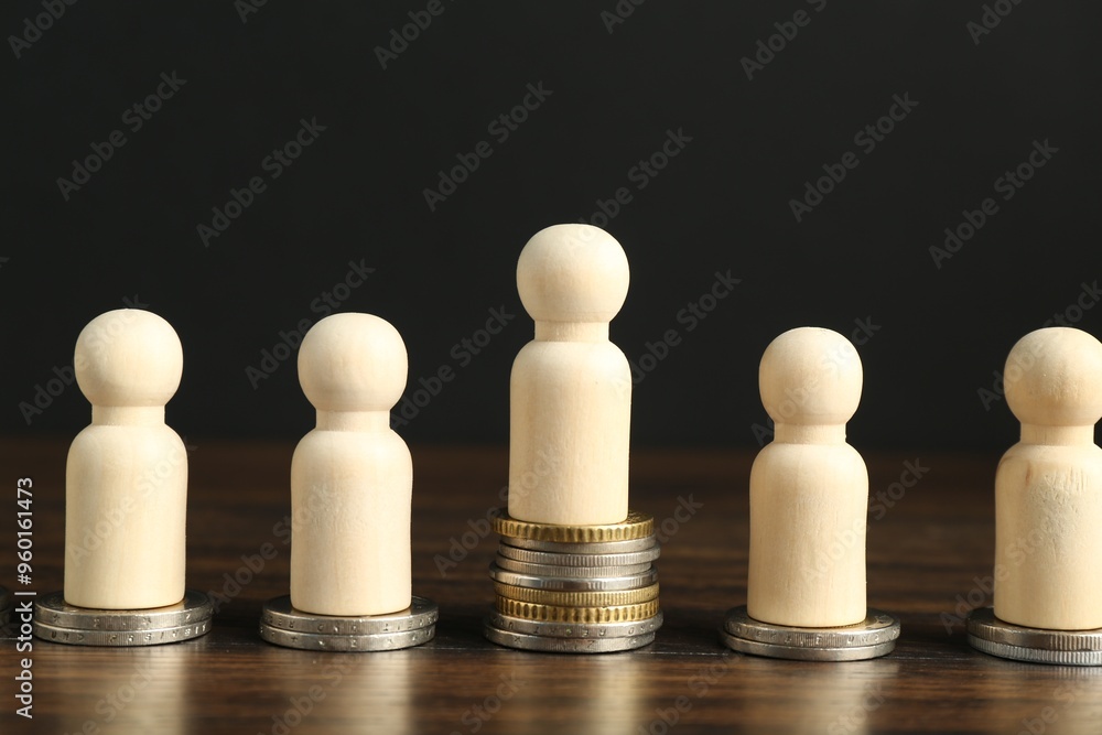 Financial inequality. One wooden figure with bigger stack of coins than others on table Financial inequality. One wooden figure with bigger stack of coins than others on table