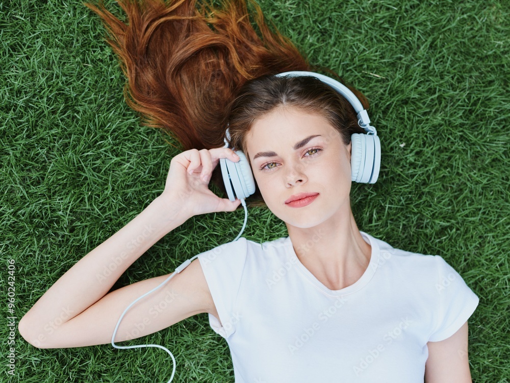 Φωτογραφία Woman portrait lying on the green grass on a sunny day listening to music in hea