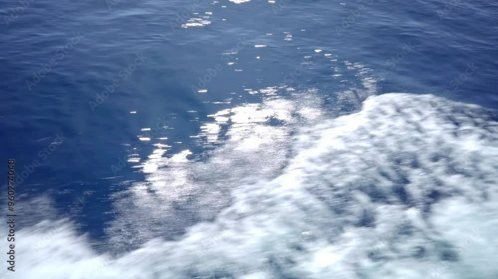 Ocean Wake, A View From the Boat. This image shows the white foam wake of a boat moving across a deep blue ocean on a sunny day, with sun reflections on the water. Ocean Wake, A View From the Boat. This image shows the white foam wake of a boat moving across a deep blue ocean on a sunny day, with sun reflections on the water.