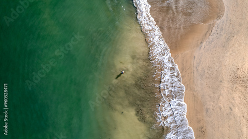 Tropical beach aerial drone top down zoom out view, bird eye view of azure waves and sand and a fisherman in the middle. Beautiful sea waves come to beach. Perspective shot.