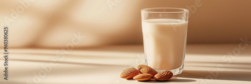 a glass of almond milk with a few almonds beside it against an isolated soft cinnamon background