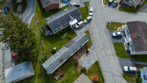 Aerial view of a suburban community shows multiple homes, with several parked vehicles and well-maintained lawns. The scene captures a typical afternoon in a quiet neighborhood setting.