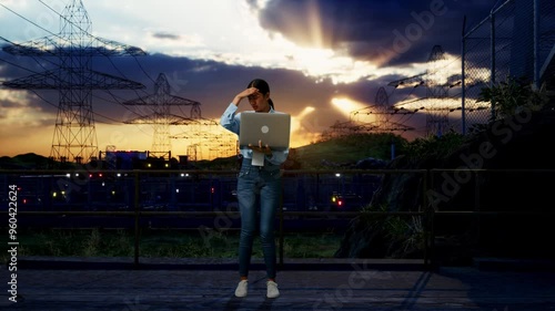 Full Body Of An Asian Female Professional Worker Standing With Her Laptop Near High Voltage Tower, Industrial Facility, She Is Nodding Her Shead With Dissapionted photo