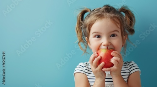 A cute little girl holding and eating a fresh ripe apple
