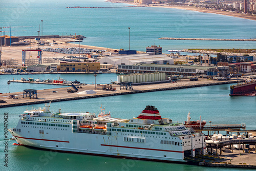 Aerial view of a ferry docked in port of Malaga city, open doors at stern of ship, industrial complex and blue ocean waters in background, sunny day in Spain photo