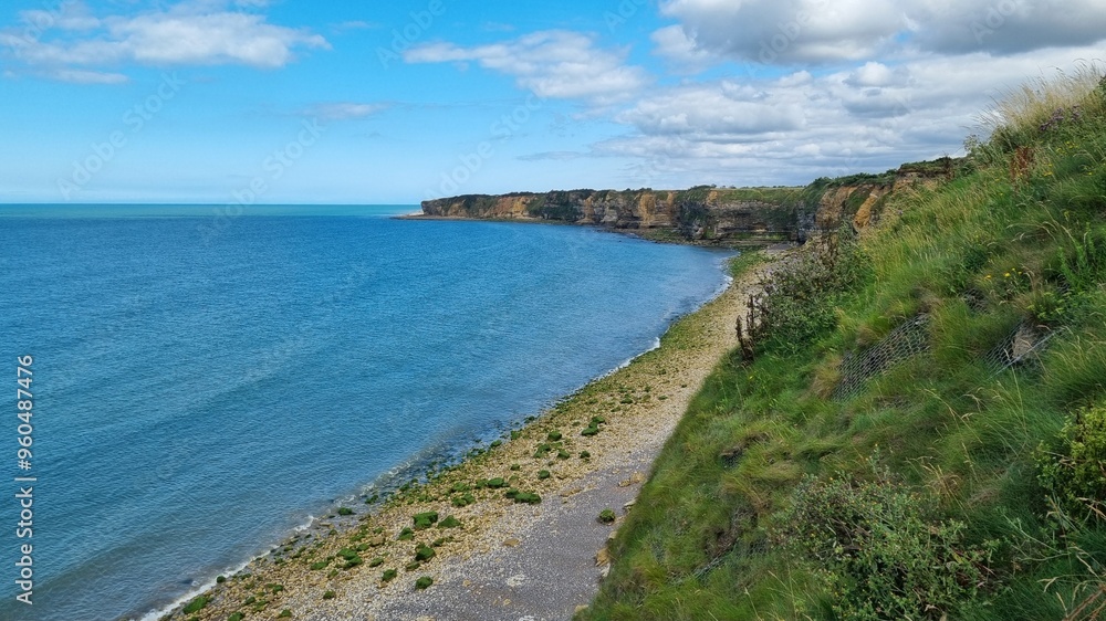 Serene coastal view of rugged cliffs and calm waters along a shoreline under a clear blue sky in daylight Serene coastal view of rugged cliffs and calm waters along a shoreline under a clear blue sky in daylight