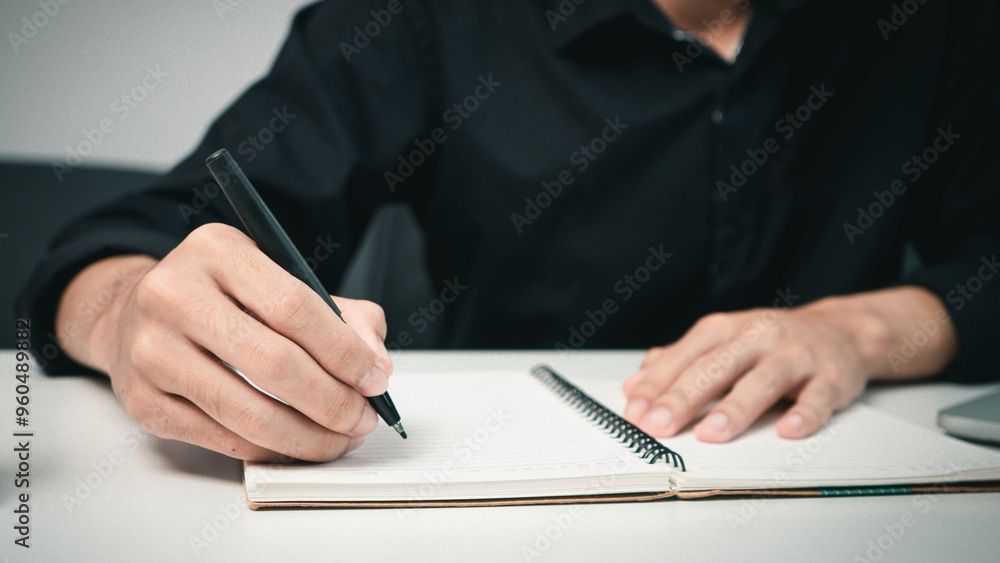 Fototapeta premium Male hand taking notes on the notepad. businessman working at work table, checklist writing planning investigate concept. focus on man hand holding pen, putting signature at official paper