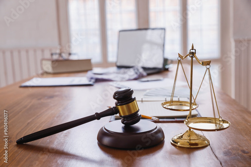 A gavel and scales of justice on a wooden desk symbolize the balance and authority of the legal system. Legal documents and a laptop reflect the modern integration of technology in law. photo