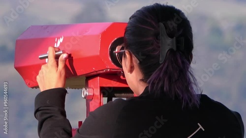 Mujer usando binoculares públicos en un mirador con paisaje de fondo