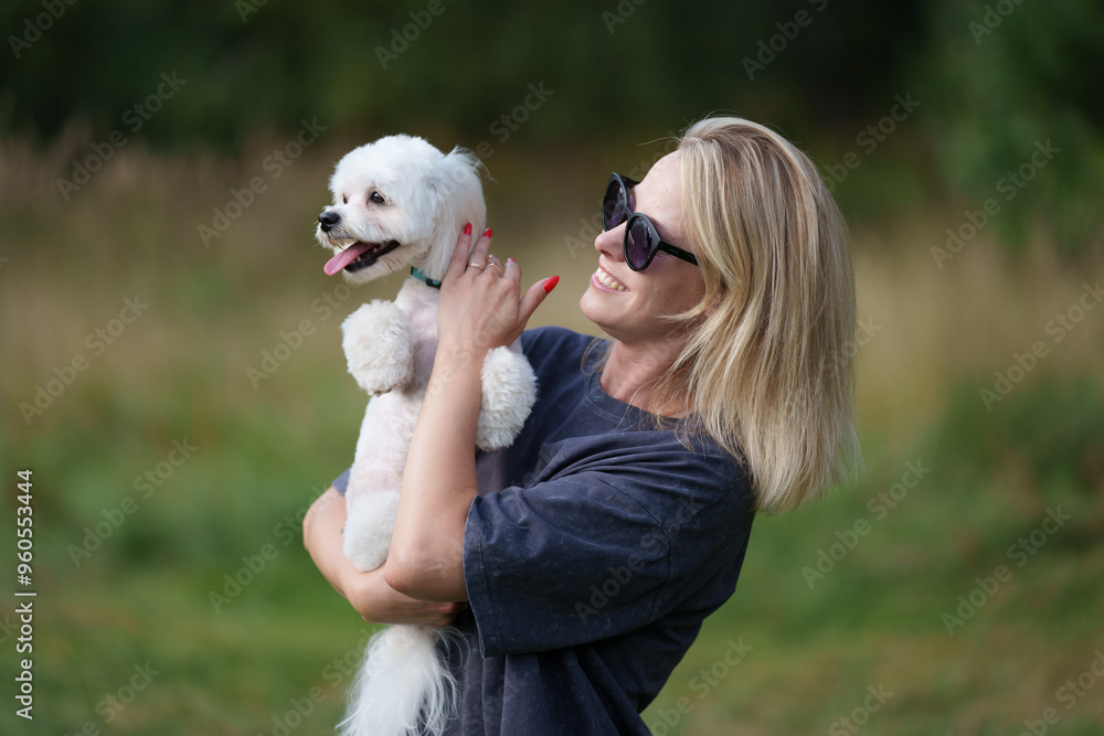 Portrait of smiling young woman kiss dog in Natural Park. Dog lover woman wearing blue dress with dog during good day. Concept of friendship and beautiful girl with a small dog Portrait of smiling young woman kiss dog in Natural Park. Dog lover woman wearing blue dress with dog during good day. Concept of friendship and beautiful girl with a small dog