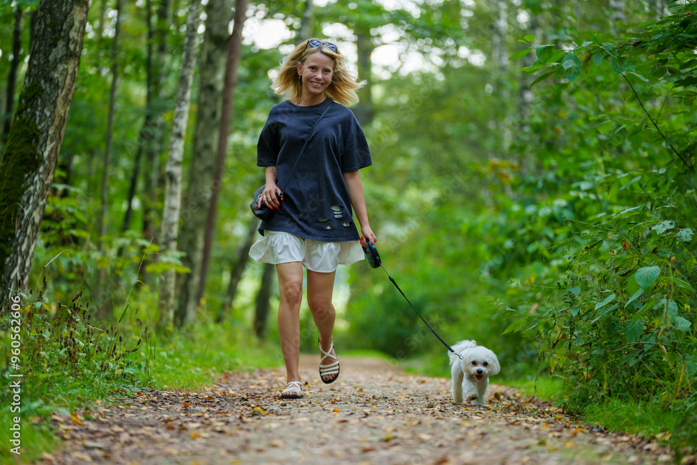 Girl walking the dog in the park forest. Rest concept. Woman walking with a dog on a leash in blue dress and with shoes. Girl walking the dog in the park forest. Rest concept. Woman walking with a dog on a leash in blue dress and with shoes.