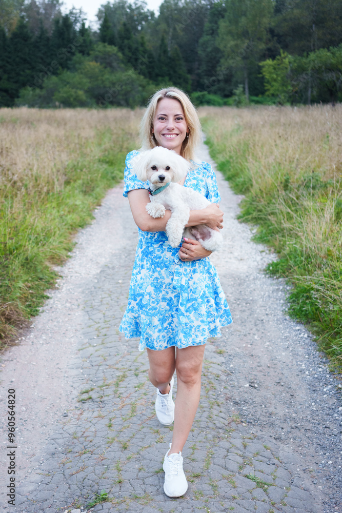 Portrait of smiling young woman kiss dog in Natural Park. Dog lover woman wearing blue dress with dog during good day. Concept of friendship and beautiful girl with a small dog Portrait of smiling young woman kiss dog in Natural Park. Dog lover woman wearing blue dress with dog during good day. Concept of friendship and beautiful girl with a small dog