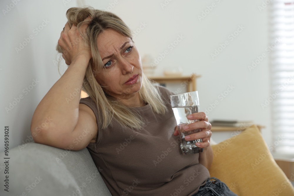 Menopause. Woman with glass of water suffering from headache on sofa at home Menopause. Woman with glass of water suffering from headache on sofa at home