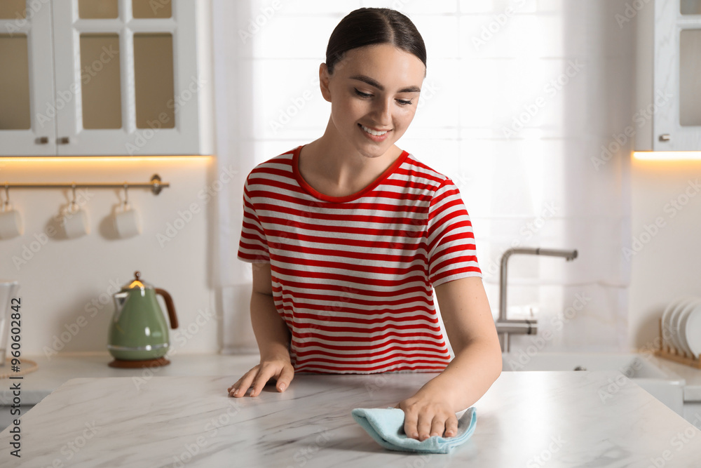 Beautiful young woman wiping white marble table with rag in kitchen Beautiful young woman wiping white marble table with rag in kitchen