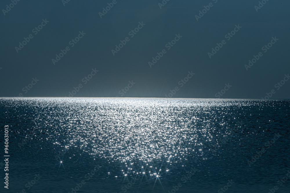 Fototapeta premium The suns light sparkles across the surface of calm ocean waters, creating a serene and shimmering horizon. The peaceful, minimalist seascape exudes tranquility with its soft reflection of light.