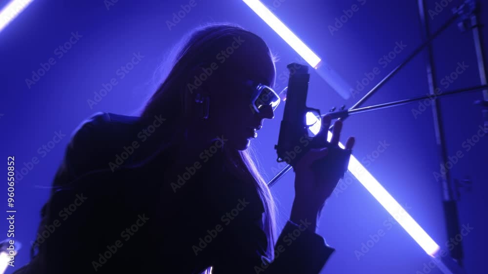 Beautiful futuristic lady in leather coat and sunglasses holding a gun and posing in a dark room lit by RGB tube lights Beautiful futuristic lady in leather coat and sunglasses holding a gun and posing in a dark room lit by RGB tube lights