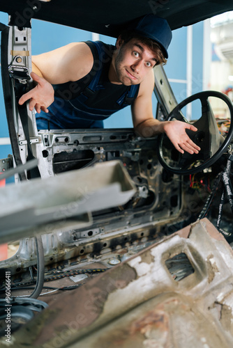 Vertical portrait of puzzled mechanic male gesturing inside disassembled car, showcasing automotive expertise and work in progress, looking at camera with puzzled emotion. Shooting in slow motion.