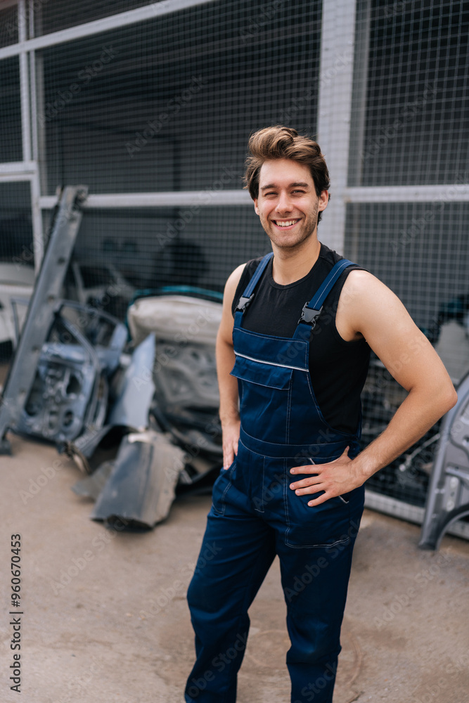 Fototapeta premium Vertical shot of cheerful male repairman in uniform standing posing in auto service shop, looking at camera with smiling expression. Concept of professional automobile maintenance in repair center.