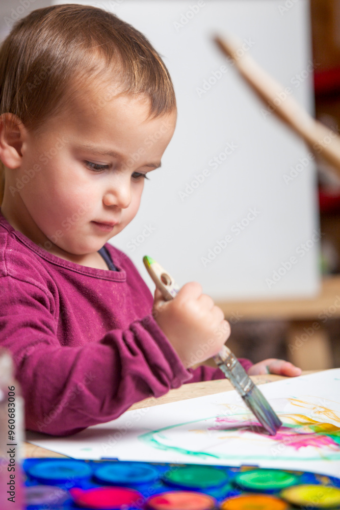 A small toddler is painting a picture on a blank piece of paper with a paintbrush. A small toddler is painting a picture on a blank piece of paper with a paintbrush.