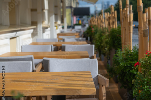 Close-up view of empty wooden tables of sidewalk cafe or street restaurant with bamboo fence in the morning. Focus on table surface. Copy space for your text or decoration. Food business theme.