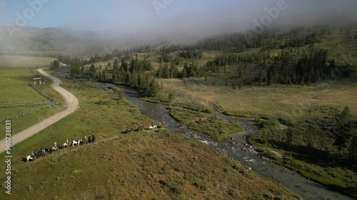 Aerial of horseback riding group crossing river in Montana mountains in summer in early morning with low clouds photo