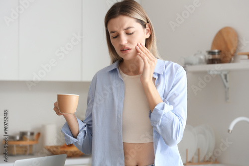 Young woman with cup of hot coffee suffering from tooth ache at home