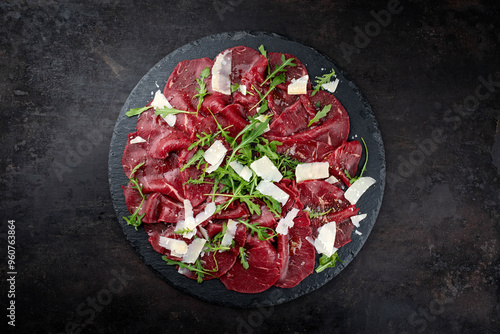 Traditional beef carpaccio served with parmesan and rocket salad as top view on a black design plate with text space