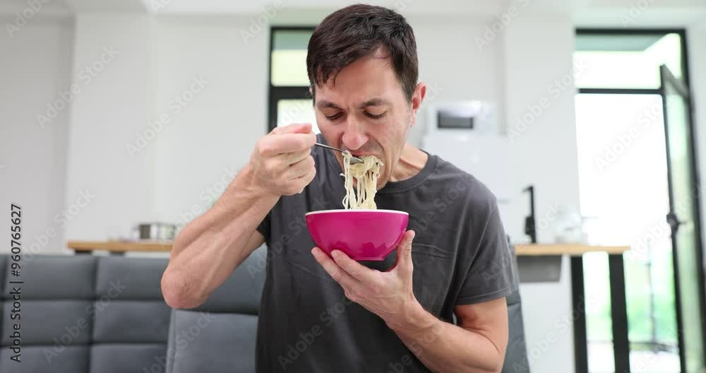 Man employee holds bowl eating instant noodles sitting in armchair in rest room in office. Guy enjoys taste of unhealthy snack during lunch Man employee holds bowl eating instant noodles sitting in armchair in rest room in office. Guy enjoys taste of unhealthy snack during lunch