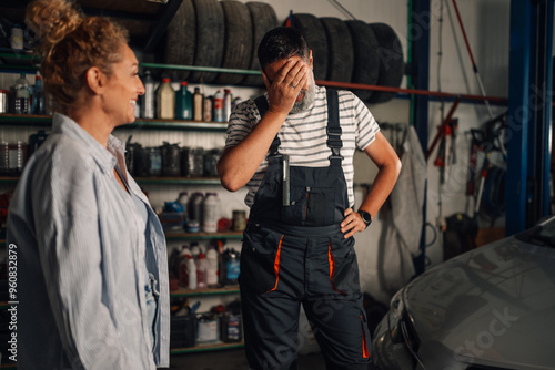 Repairman is doing facepalm at mechanic workshop and standing near car