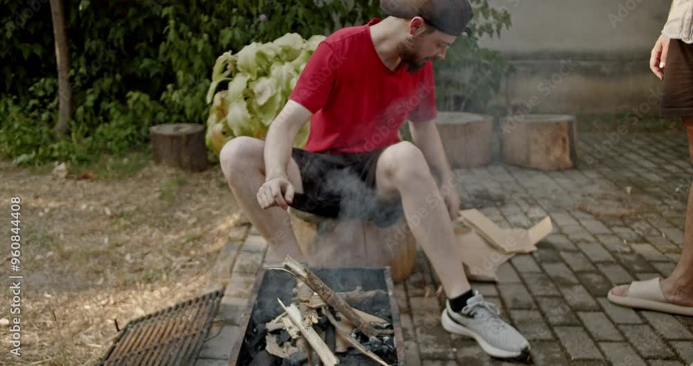 Friends getting ready for a barbecue in the yard. One man is arranging the wood in the barbeque to get the fire going. Friends getting ready for a barbecue in the yard. One man is arranging the wood in the barbeque to get the fire going.