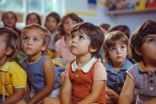 Group of small nursery school children sitting and listening to teacher on floor indoors in classroom.