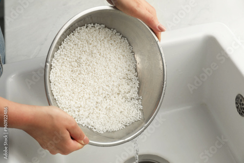 Woman rinsing rice in bowl above sink, closeup