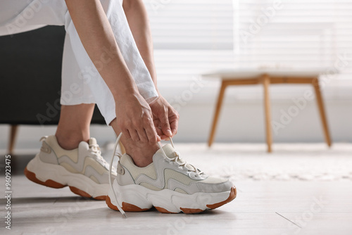 Картината върху платно Woman tying shoelace of sneaker indoors, closeup. Space for text
