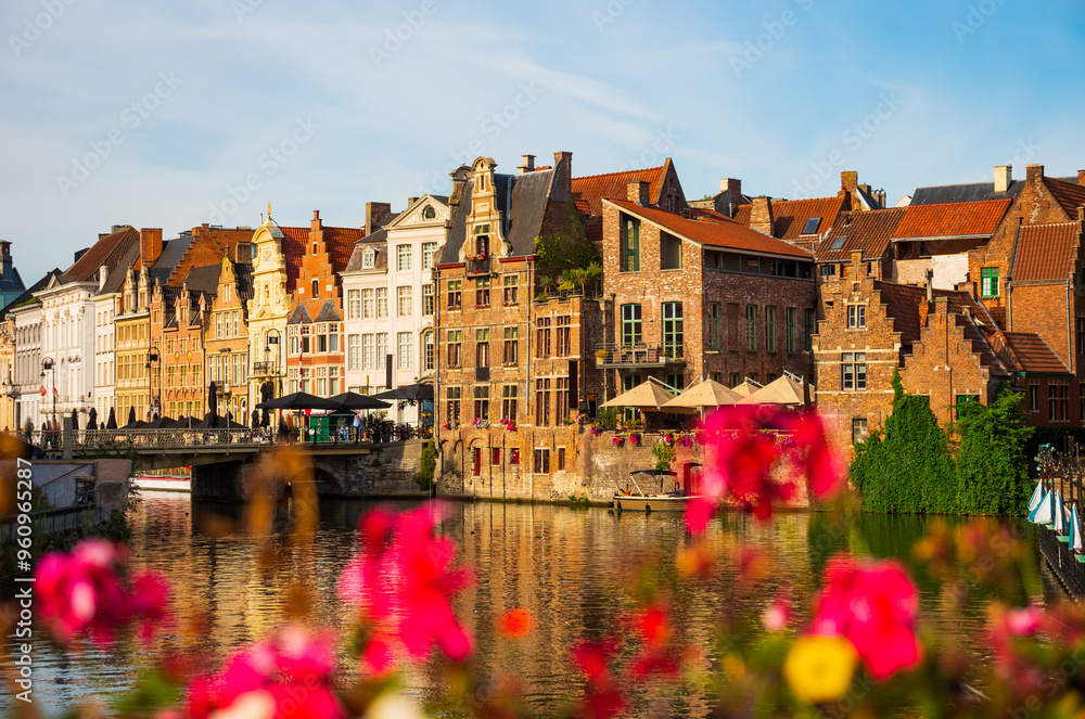 Obraz premium View of picturesque blooming area with typical residential buildings in historic center of Ghent city along Leie river on summer day, Belgium