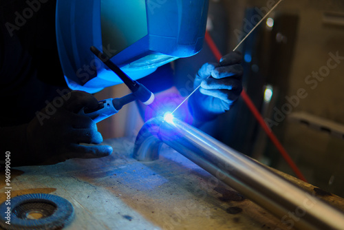 A man is welding a pipe with a blue light