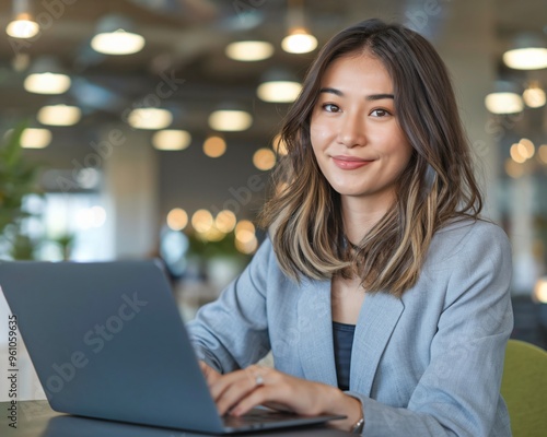 A photo of a young Asian woman with shoulder-length loose wave brunette hair, wearing a gray blazer.