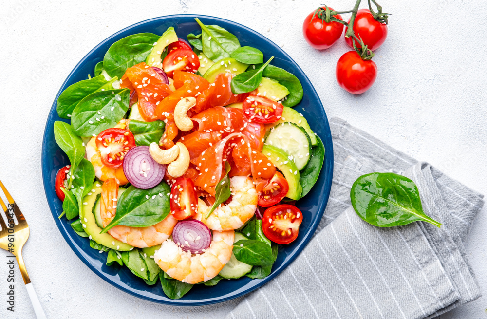 Seafood salad with shrimp, salmon, avocado, spinach, cucumber, tomato, cashew and sesame seeds.. White background, top view Seafood salad with shrimp, salmon, avocado, spinach, cucumber, tomato, cashew and sesame seeds.. White background, top view