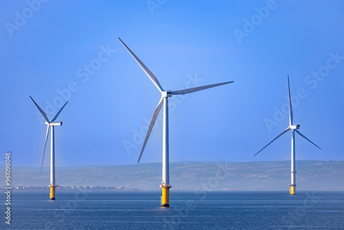 Abstract ethereal view of beautiful giant wind turbines at sea with patchy fog blue sky