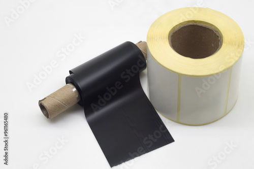 Black roll wax ribbon for thermal transfer on core and white self-adhesive label roller for a special barcode printer. Consumables and auxiliary materials for barcode printing. Selective focus