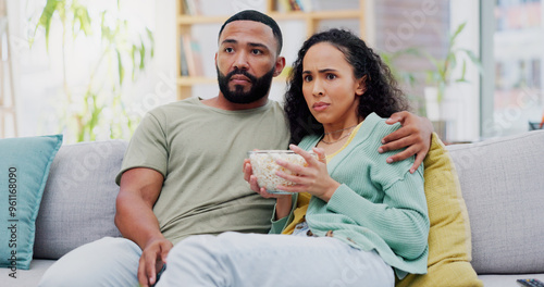 Tableau sur toile Couple, scared and watching tv on sofa with popcorn in home for horror film, streaming and hug in living room