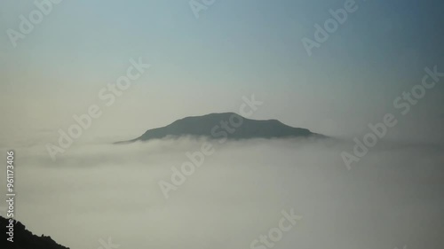 A mountain top surrounded by slow moving clouds. Above it is a blue sky. Recorded at an elevation of 1,200 meters above sea level, atop a mountain in Peru called Apu Siqay. photo