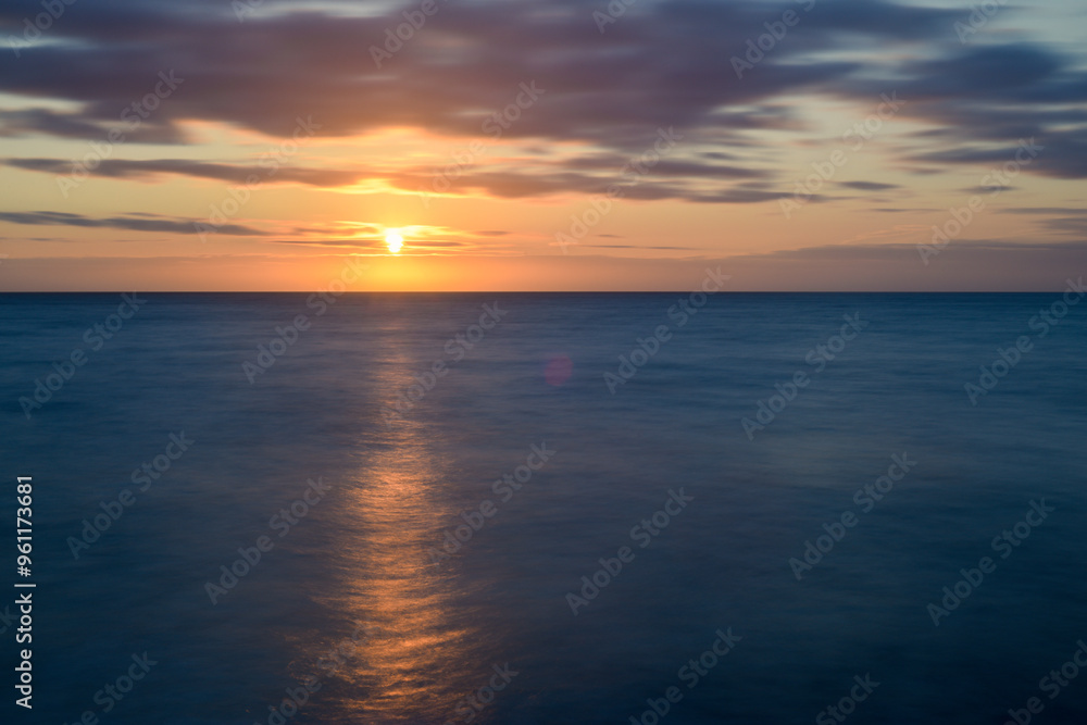 sunset over calm ocean water as the evening light reflects over the sea sunset over calm ocean water as the evening light reflects over the sea